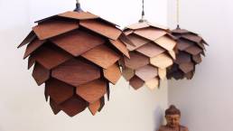 Pinecone Lamp Wood. In a white room with a buddha statue. we see three different tones of the suspended wooden picone lamp. omeech